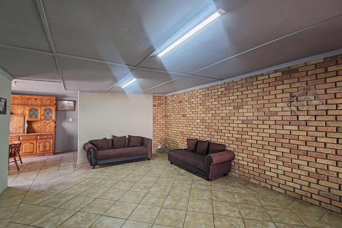 Spacious living area featuring an exposed brick feature wall, tiled flooring, and functional fluorescent lighting, offering a blank canvas for renovation.