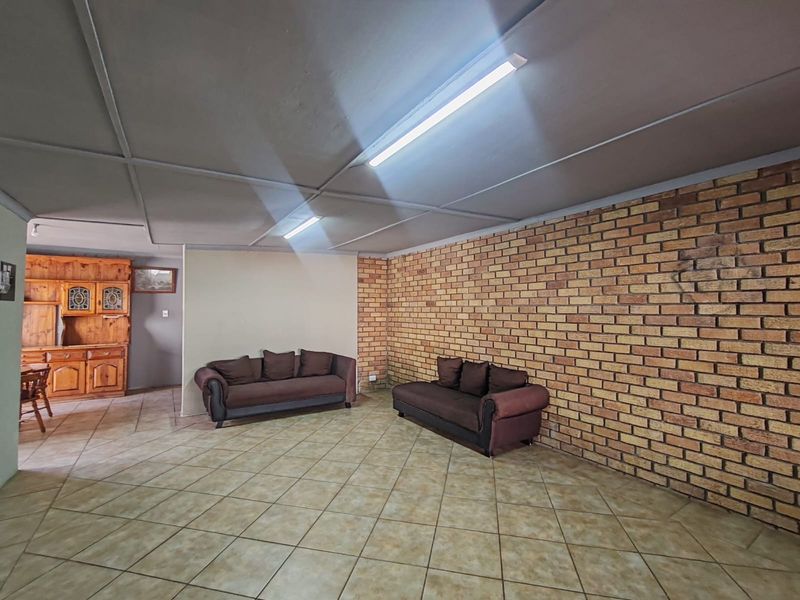 Spacious living area featuring an exposed brick feature wall, tiled flooring, and functional fluorescent lighting, offering a blank canvas for renovation.