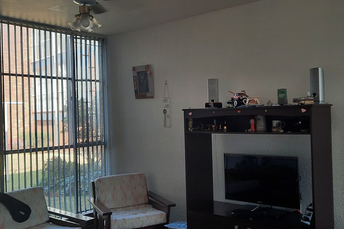 A living room area featuring a large window with security bars and a ceiling fan, providing natural light and a view of the exterior.