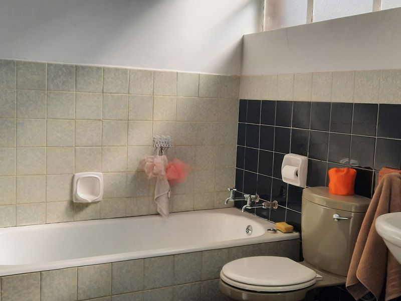 A functional bathroom featuring a bathtub, pedestal basin, and toilet with dated wall tiling.