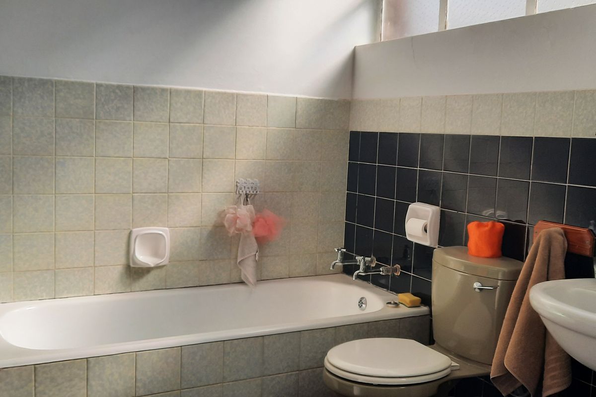 A functional bathroom featuring a bathtub, pedestal basin, and toilet with dated wall tiling.