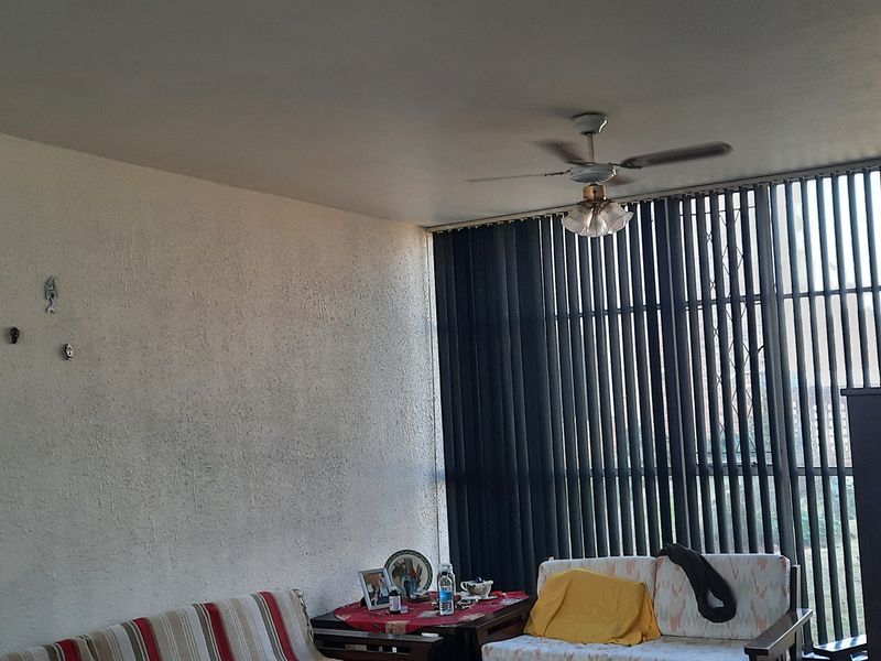 A living room area featuring a ceiling fan and floor-to-ceiling vertical blinds, providing natural light and a view of the exterior.