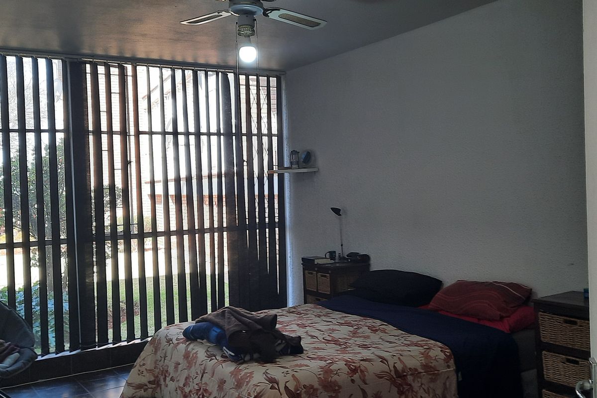 A bedroom featuring tiled flooring, a ceiling fan, and large windows with vertical blinds providing natural light.