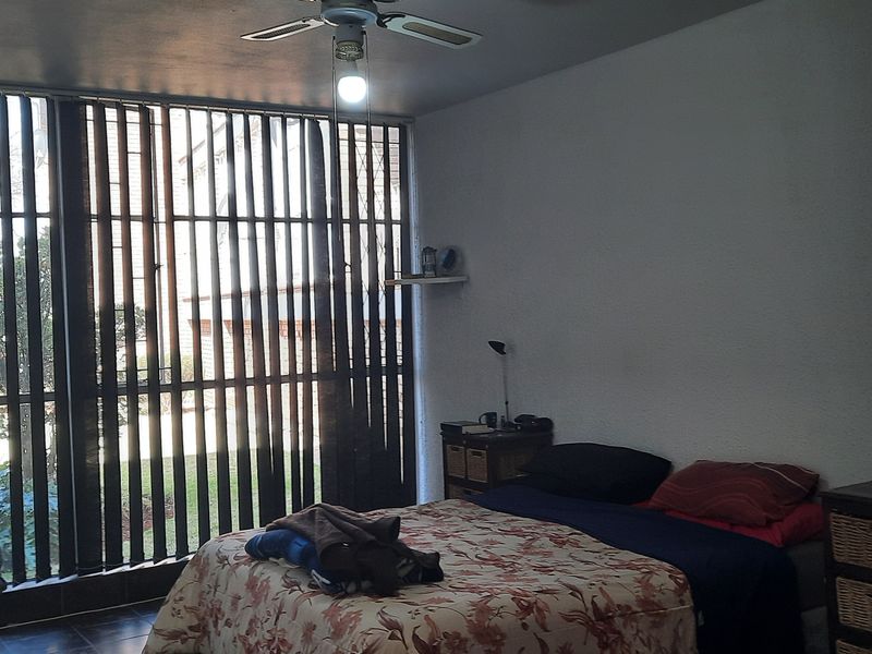 A bedroom featuring tiled flooring, a ceiling fan, and large windows with vertical blinds providing natural light.