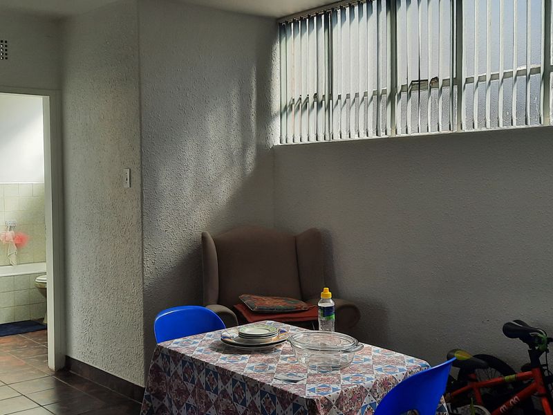 A living area featuring textured walls, tiled flooring, and high-level windows with vertical blinds, providing access to an adjacent bathroom.