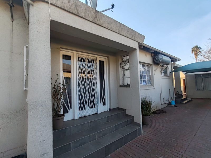 Front entrance of the flat featuring tiled steps, a security gate, and an exterior solar geyser unit mounted on the wall.