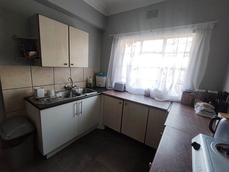 A functional kitchen featuring laminate cabinetry, a double bowl stainless steel sink, and tiled splashbacks, offering a practical layout with natural light.