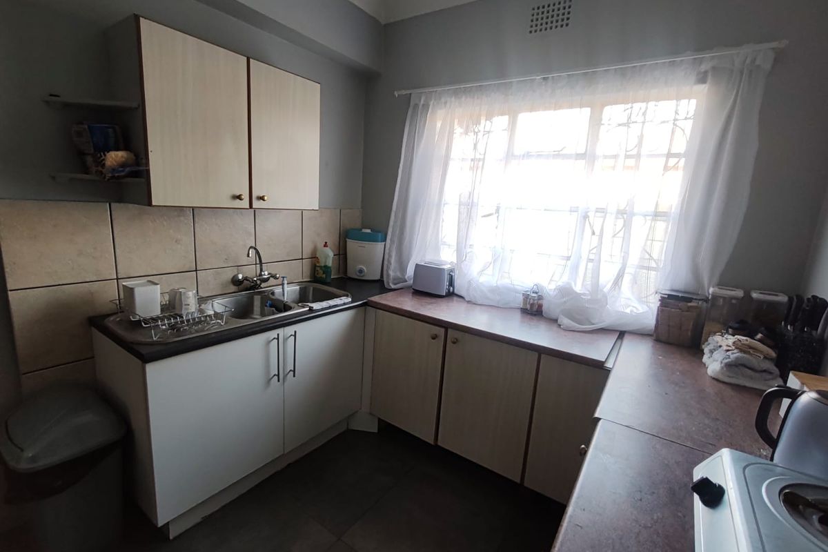 A functional kitchen featuring laminate cabinetry, a double bowl stainless steel sink, and tiled splashbacks, offering a practical layout with natural light.