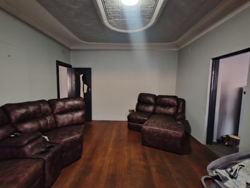 A living room featuring original hardwood flooring and an ornate decorative ceiling rose with matching cornice detailing.