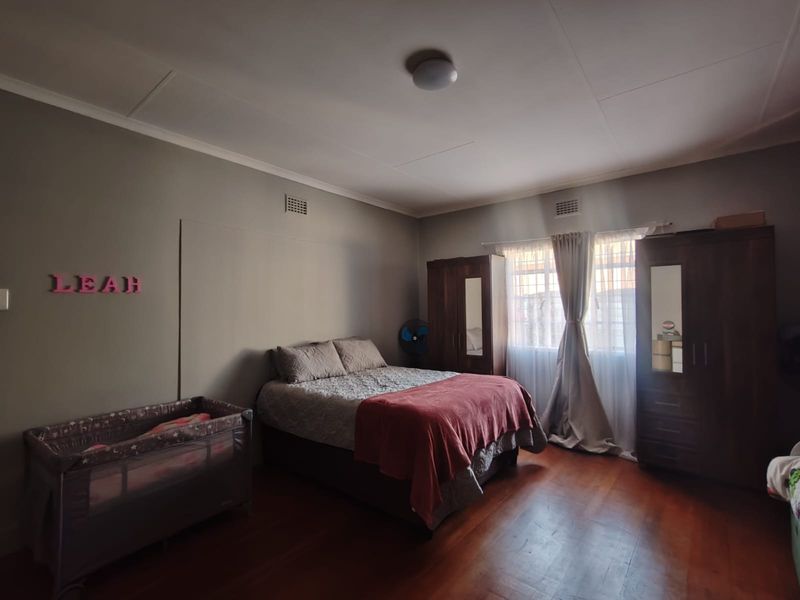A spacious bedroom featuring warm timber flooring, neutral wall tones, and natural light through a window with fitted curtains.