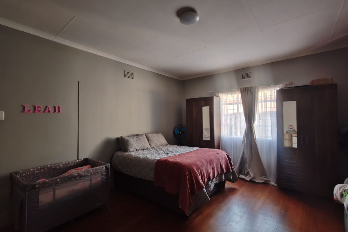 A spacious bedroom featuring warm timber flooring, neutral wall tones, and natural light through a window with fitted curtains.