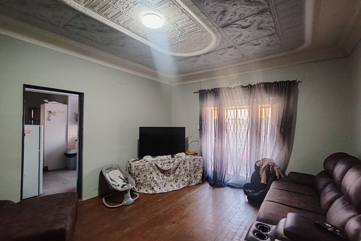 Living room featuring a distinctive ornate pressed metal ceiling, timber flooring, and access to an outdoor area through a sliding glass door with security gate.