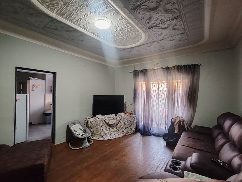 Living room featuring a distinctive ornate pressed metal ceiling, timber flooring, and access to an outdoor area through a sliding glass door with security gate.