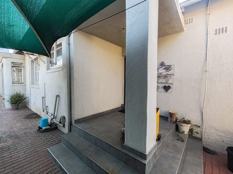 A covered patio area featuring tiled steps, a structural concrete pillar, and overhead shade sail, providing a functional outdoor transition space.