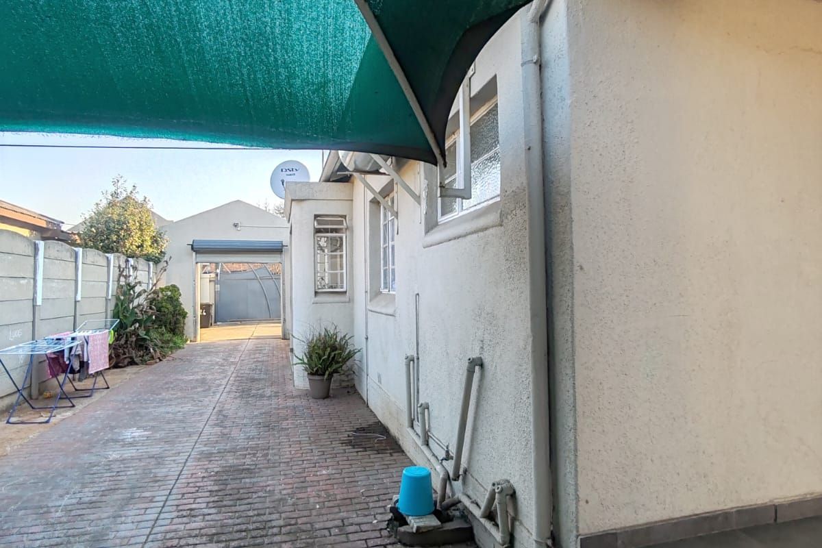 Rear exterior area featuring a paved driveway, shade sail covering, and concrete boundary wall, providing access to the property entrance.