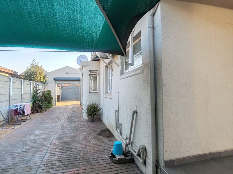 Rear exterior area featuring a paved driveway, shade sail covering, and concrete boundary wall, providing access to the property entrance.