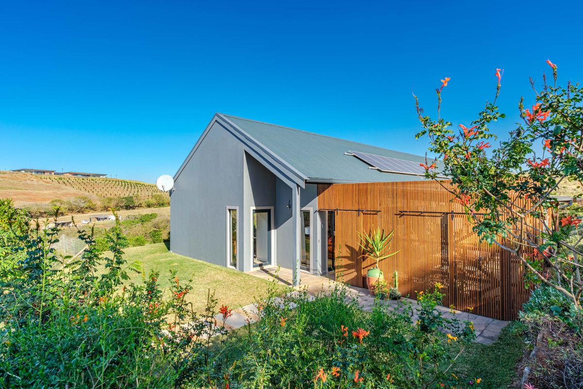 Modern rear exterior view featuring a metal roof with solar panels, a timber slat privacy screen, and a paved patio area overlooking the landscape.