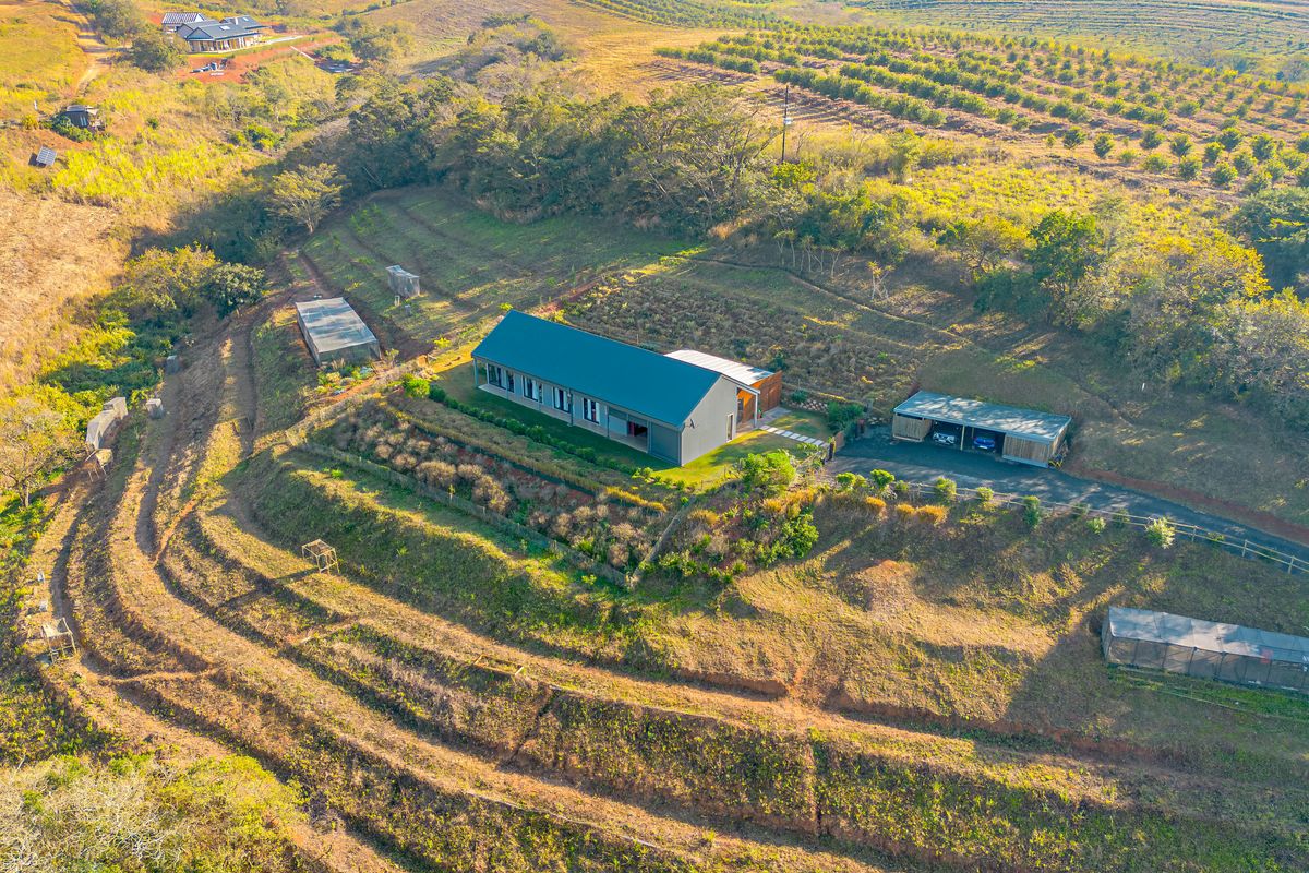 Aerial view of a modern rural property featuring a main residence, detached garage, and extensive terraced grounds set within a scenic landscape.