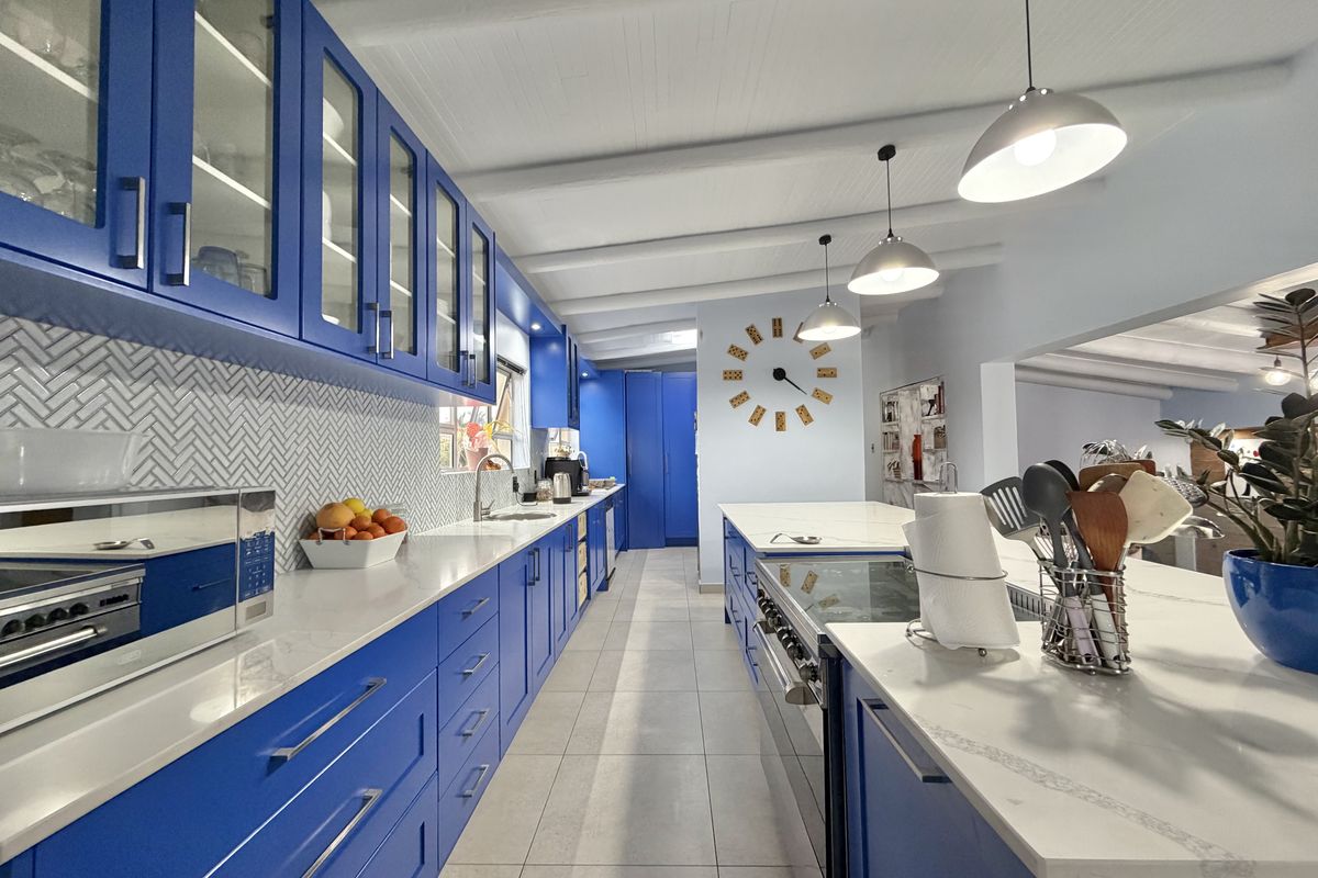 Modern kitchen featuring vibrant blue cabinetry, stone countertops, a large central island with a gas range, and stylish herringbone tile backsplash.
