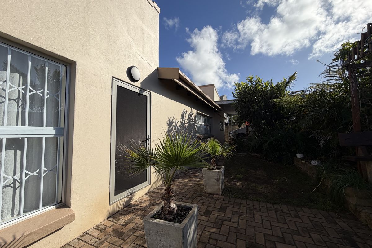 A rear exterior view of the property featuring a paved patio area, security gate, and window security bars.