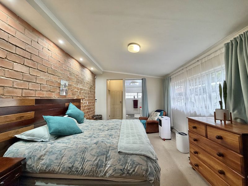 Spacious bedroom featuring an exposed brick feature wall, recessed lighting, and direct access to an en-suite bathroom.