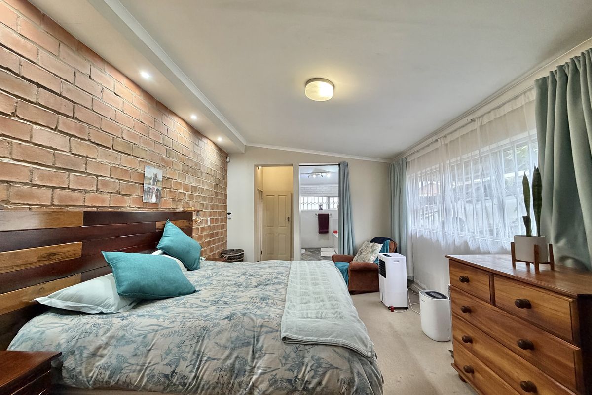 Spacious bedroom featuring an exposed brick feature wall, recessed lighting, and direct access to an en-suite bathroom.