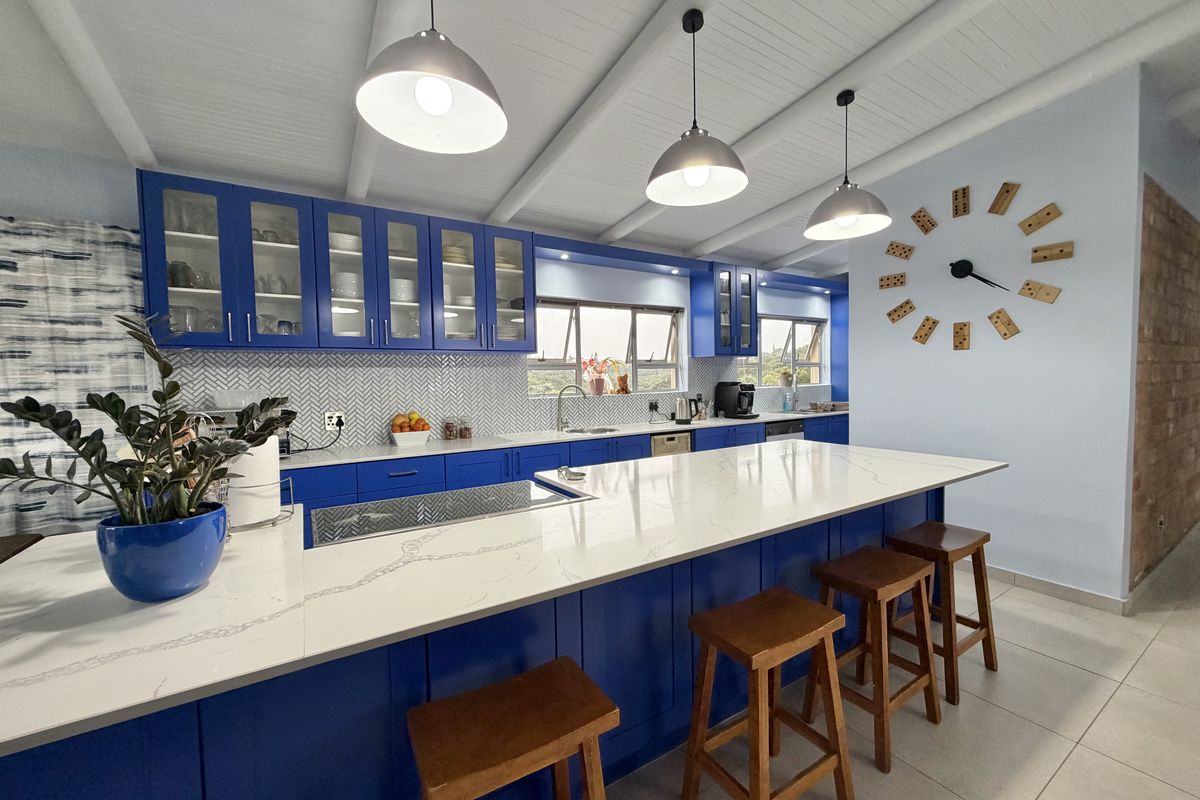 Modern kitchen featuring vibrant blue cabinetry, a large quartz-topped island, herringbone backsplash, and exposed beam ceilings, creating a bright and functional culinary space.