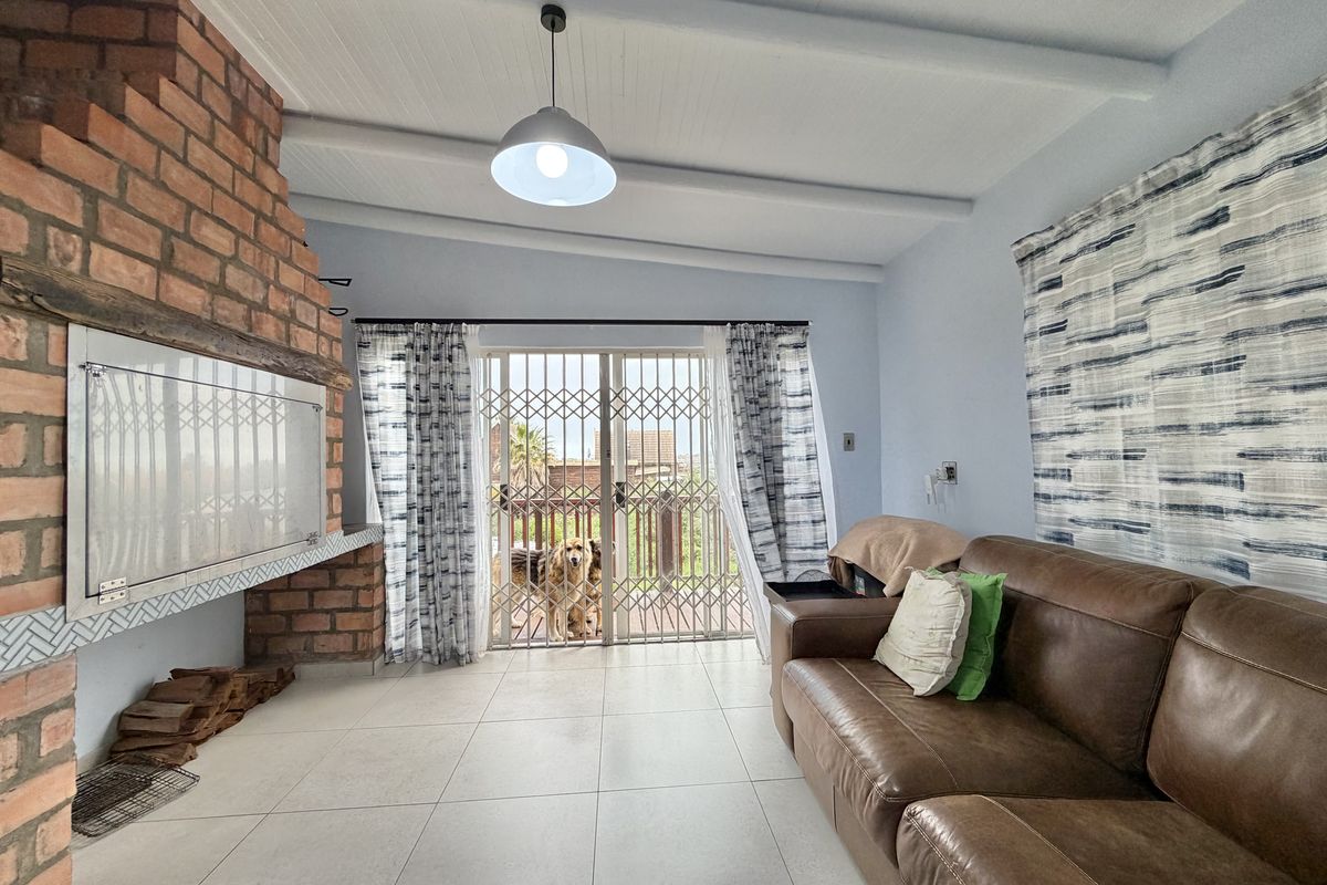 Living room featuring an exposed brick fireplace, tiled flooring, and exposed beam ceiling, with direct access to an outdoor area through sliding glass doors.