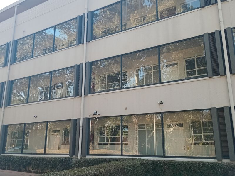 A multi-story apartment building facade featuring large glass windows, external security lighting, and a well-maintained hedge along the front.