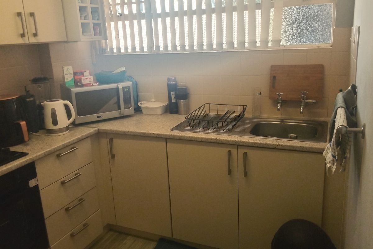 A functional kitchen featuring laminate cabinetry, a stainless steel sink, built-in oven, and tiled backsplash with natural light from a window.