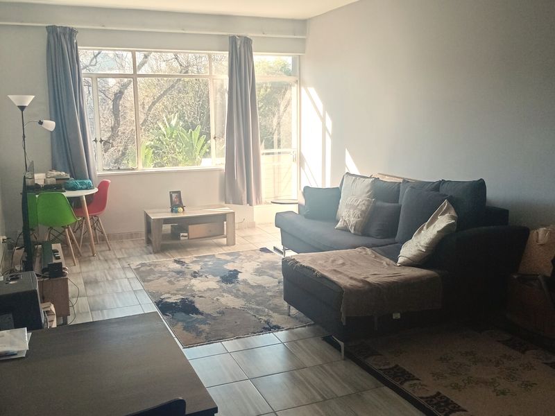 A bright, open-plan living area featuring tiled flooring, large windows providing natural light, and direct access to an outdoor space.