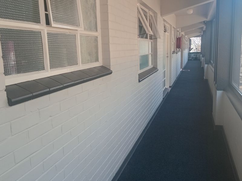 An exterior apartment walkway featuring painted brick walls, tiled window sills, and large windows overlooking the street.