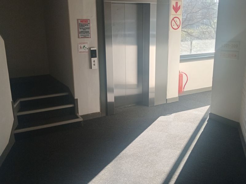 A communal hallway area featuring a stainless steel elevator, carpeted flooring, and access to a staircase.