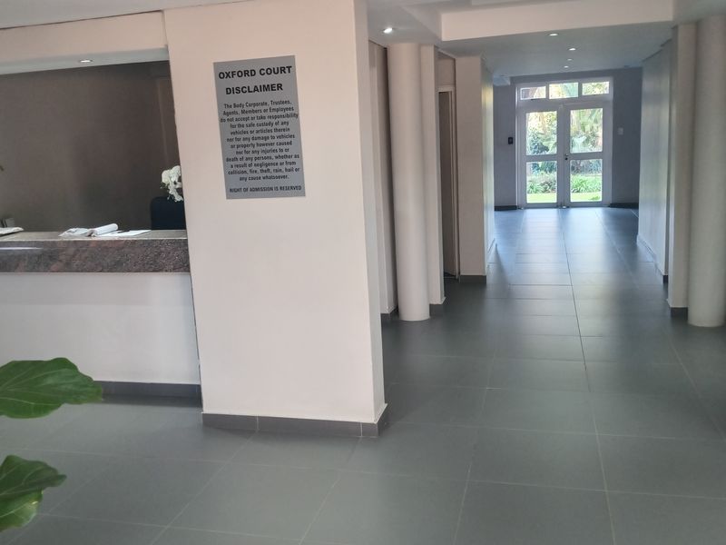 A clean and well-maintained building entrance lobby featuring tiled flooring, a reception desk, and glass double doors leading to the exterior.
