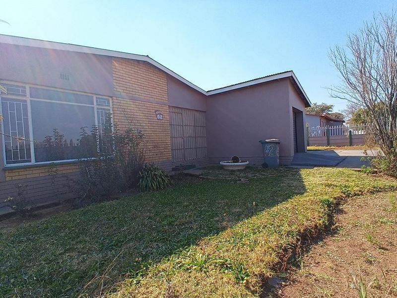 Front elevation of a single-story brick house featuring a driveway, attached garage, and security gate entrance.