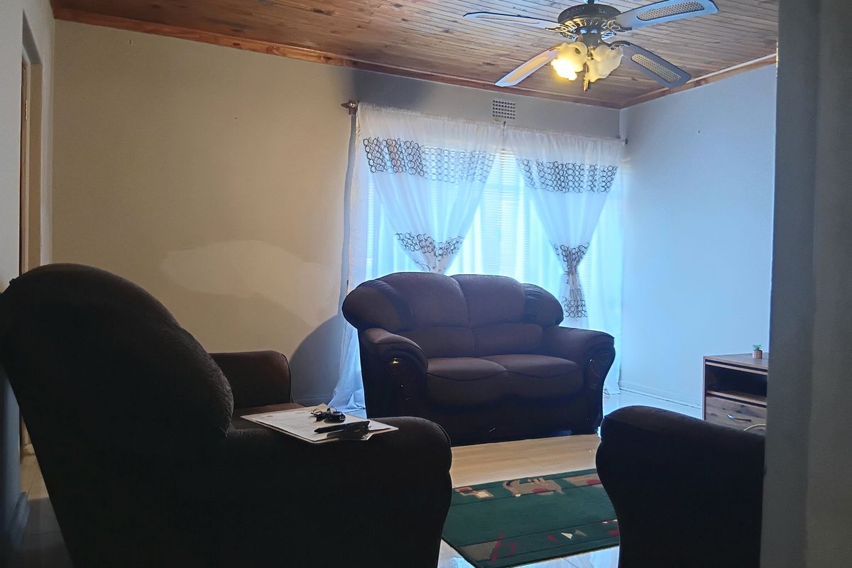 A living room featuring a timber-clad ceiling, ceiling fan, and tiled flooring, with visible wall paint patches requiring attention.