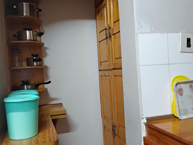 A compact scullery area featuring built-in wooden cabinetry, open shelving, and a tiled splashback, accessed through a traditional arched doorway.