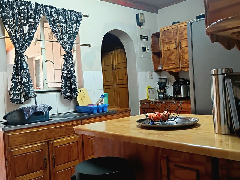 A dated kitchen featuring wooden cabinetry, a timber ceiling, and a breakfast counter, with an arched doorway leading to adjacent living spaces.