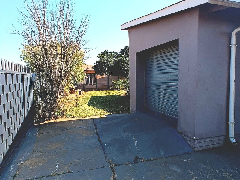 Exterior view of a single garage with a roller shutter door and a cracked concrete driveway leading to a rear garden area.