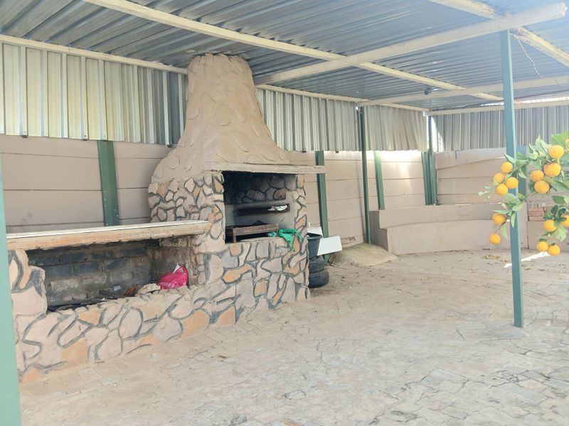 Covered outdoor patio area featuring a large built-in stone braai and fireplace, providing a functional space for outdoor entertaining.