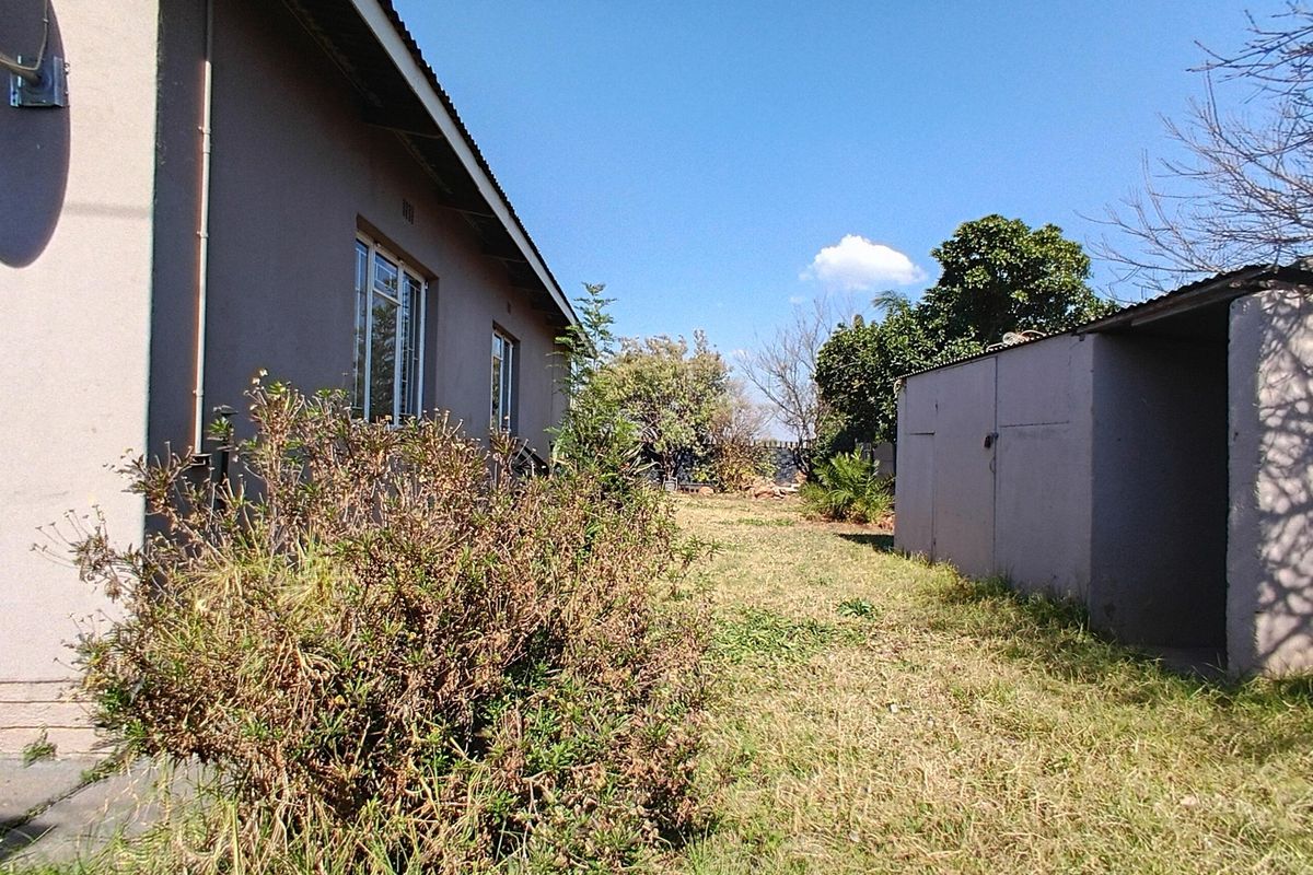 Rear view of the property showing the main house structure, a detached outbuilding, and a large backyard area with grass.