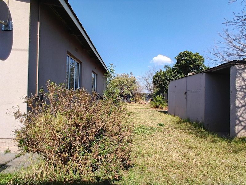 Rear view of the property showing the main house structure, a detached outbuilding, and a large backyard area with grass.