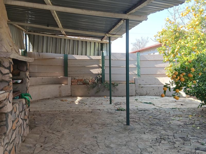 Covered outdoor patio area featuring a stone-clad built-in braai, paved flooring, and integrated concrete seating, offering a functional space for outdoor entertaining.
