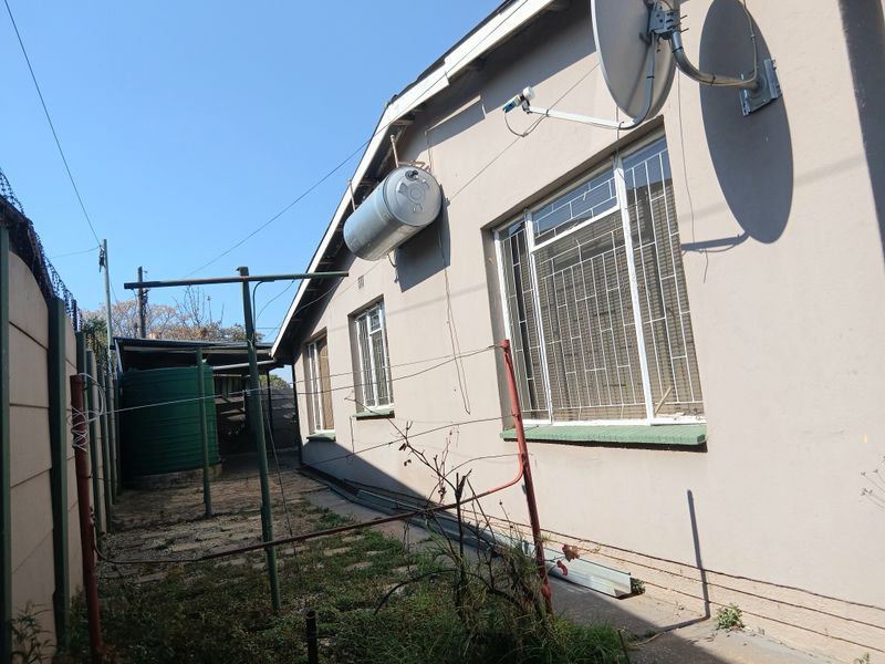 Rear exterior view of the property featuring a solar geyser, water tank, security bars on windows, and a paved utility area.