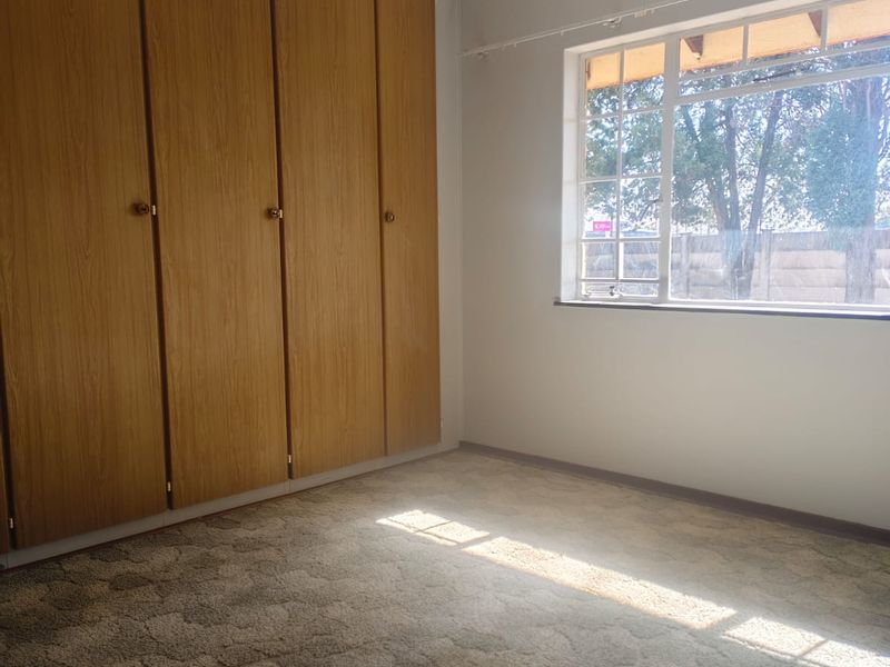 A vacant bedroom featuring built-in wooden cupboards, carpeted flooring, and a window with security bars, offering a blank canvas for personalization.