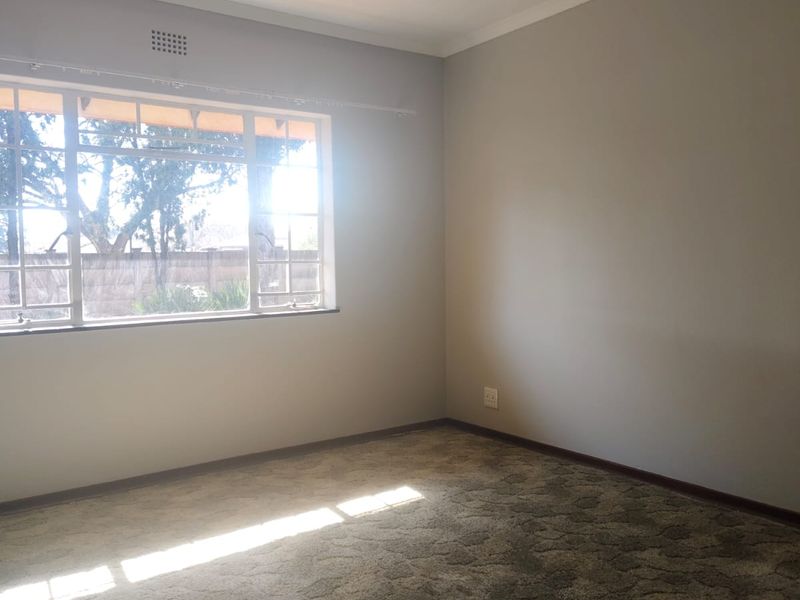A vacant bedroom featuring neutral wall paint, carpeted flooring, and a window with security bars, providing a blank canvas for personalization.