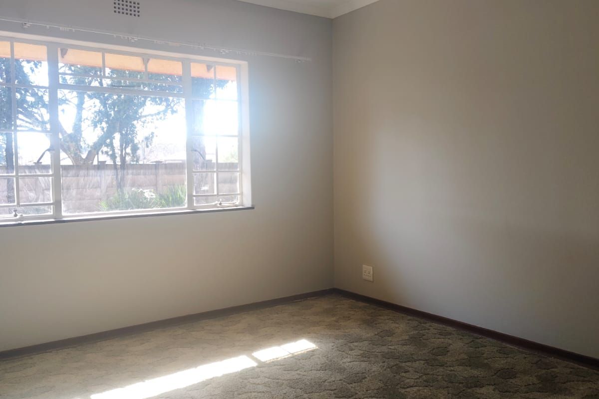 A vacant bedroom featuring neutral wall paint, carpeted flooring, and a window with security bars, providing a blank canvas for personalization.