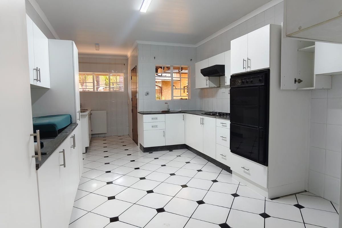 A spacious kitchen featuring white cabinetry, black countertops, a built-in oven, and distinctive black and white tiled flooring.