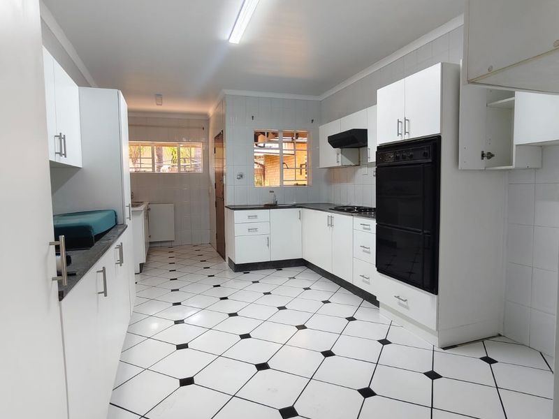 A spacious kitchen featuring white cabinetry, black countertops, a built-in oven, and distinctive black and white tiled flooring.