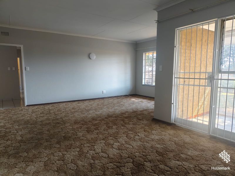 An empty living room featuring carpet flooring, coving, and a security gate leading to an outdoor area.